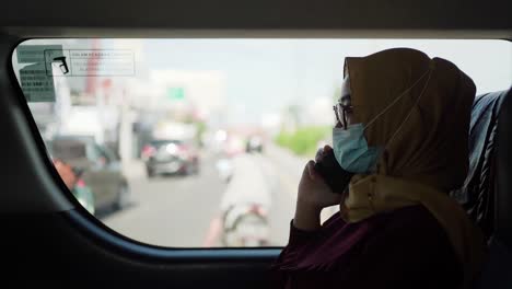 Woman-wearing-mask-talking-by-phone-while-sitting-in-taxi