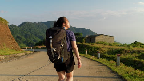slow-motion-of-solo-female-traveller-with-backpack-walking-on-rural-countryside-during-a-sunny-day-with-panoramic-mountains-view