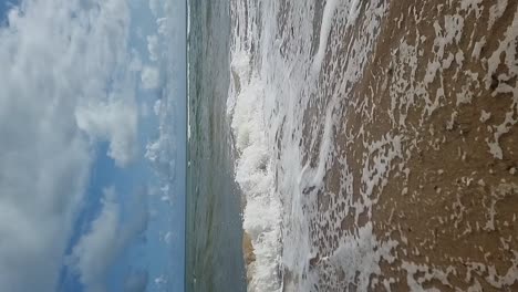 VERTICAL-Slow-motion-Tropical-ocean-waves-flowing-across-golden-sandy-beach-under-blue-cloudy-sky