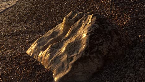 Natural-sculpture-on-shoreline-of-Mediterranean,-beautiful-carved-rock-plunged-on-beach-reflecting-sunlight-at-golden-hour