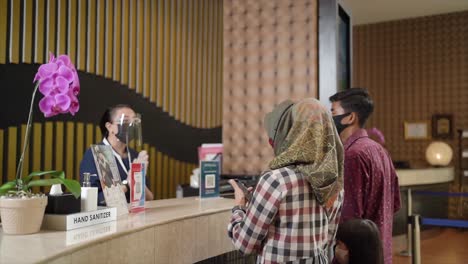 Smiling-family-of-three-enters-to-the-hotel-lobby-to-check-in-at-the-reception-for-vacation