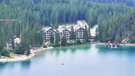 Hotel-complex-near-beautiful-Dolomite-lake,-forest-background