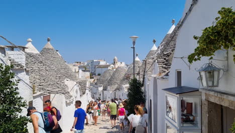 Calle-Concurrida-Con-Muchos-Turistas-Caminando-Entre-Las-Casas-Trulli-Con-Techos-Cónicos-En-Alberobello-Puglia-Italia