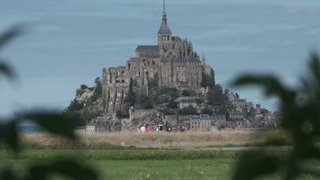 Mont-Saint-Michel-island-in-Normandy,-France-with-people-walking-on-grass-in-front
