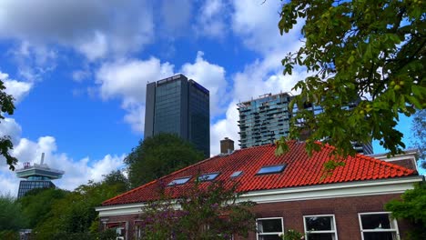 Contrast-between-old-traditional-cute-Dutch-house-with-orange-roof-and-modern-skyline-apartment-blocks