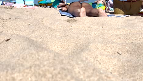fit-woman-in-a-black-bikini-sunbathes-amidst-a-crowd-in-Portugal,-enjoying-the-sun