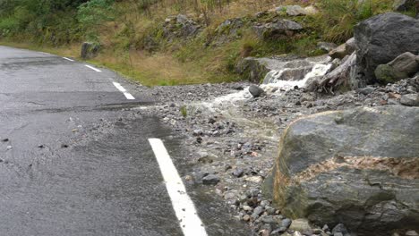 Water-flowing-from-hillside-into-road-and-over-white-road-marking---Closeup-of-water-flowing-over-asphalt