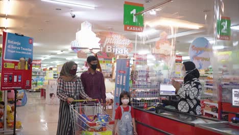 Young-family-standing-at-checkout-buying-groceries-in-supermarket