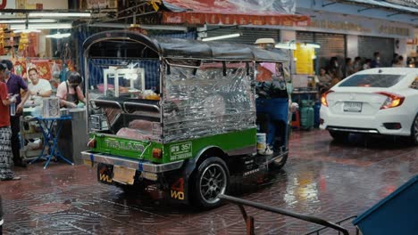 Tuk-Tuk-taxi-at-a-rainy-evening-in-the-city-of-Bangkok,-Thailand-driving-through-the-street