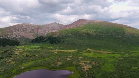 Drone-pullback-tilt-up-reveals-white-fluffy-clouds-above-scenic-lush-green-rolling-hills-of-guanella-pass,-colorado
