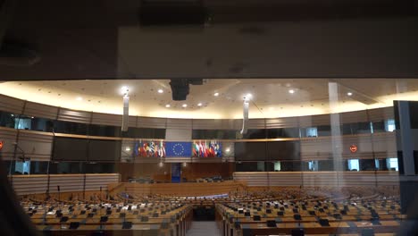 POV-Walking-Towards-Round-Glass-Window-Showing-Empty-Plenary-Hall-At-The-European-Parliament-Looking-Towards-Main-Stage-Located-In-Brussels,-Belgium