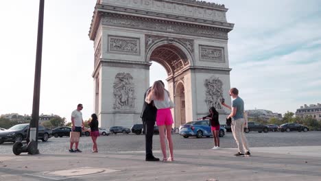 Turistas-Posando-Para-Fotos-En-El-Arco-Del-Triunfo-En-París-Durante-La-Puesta-De-Sol:-Momentos-Capturados,-Atmósfera-De-La-Hora-Dorada,-Emblemático-Monumento-Francés,-Luz-Nocturna