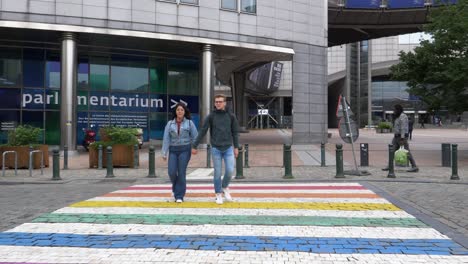 Junges-Paar-überquert-Regenbogenfarbenen-Übergang-Vor-Dem-Gebäude-Des-Europäischen-Parlaments-In-Brüssel
