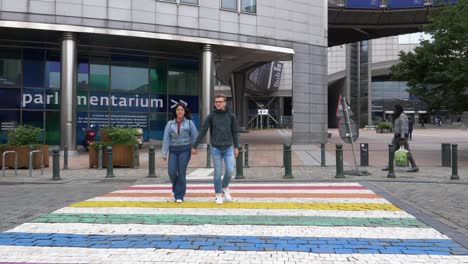 Pareja-Joven-Cruzando-El-Cruce-De-Colores-Del-Arco-Iris-Fuera-Del-Edificio-Del-Parlamento-Europeo-En-Bruselas