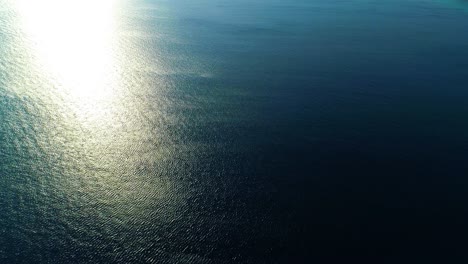 Aerial-panoramic-overview-of-deep-blue-water-and-bright-plume-of-warm-sunlight-on-ocean-shimmering