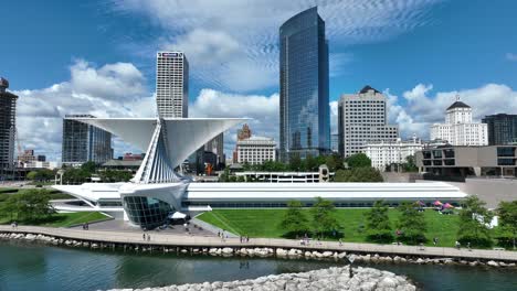 Descending-aerial-shot-of-Milwaukee-skyline,-art-museum,-and-Lake-Mighigan-on-beautiful-summer-day-with-blue-sky-and-clouds