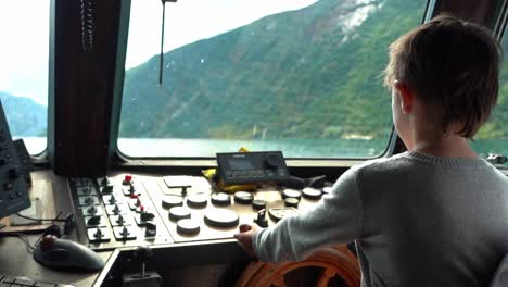 7-Year-old-boy-steering-a-boat-with-the-helmsman-steering-wheel-inside-wheelhouse---Slow-motion-seen-from-behind