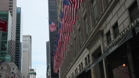 Tilt-down-shot-of-many-American-flags-lined-up-outside-buildings-in-downtown-of-New-York-City,-USA