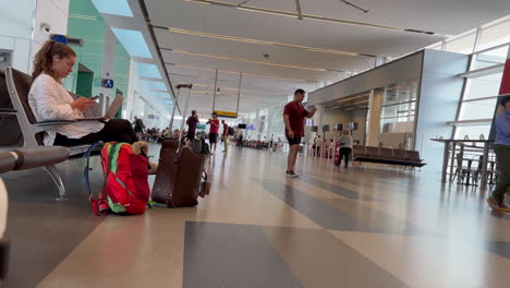 Caucasian-Woman-Sitting-at-Boarding-Area-With-Luggage,-Using-Mobile-Phone-and-Laptop-at-Calgary-YYC-Airport-on-7-18-2023