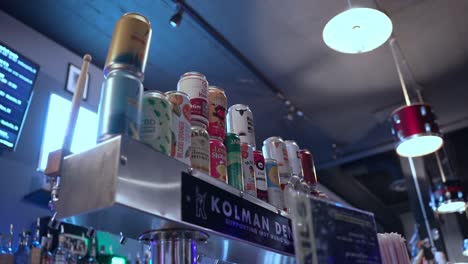 Counter-of-a-bar-with-colorful-drinks-in-cans-and-behind-lamps