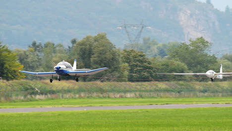 Glider-plane-taking-off-with-aerotow-and-pilot-waving-from-cockpit,-tracking-shot