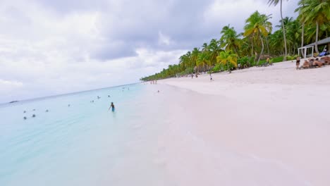 FPV-Estableciendo-Vuelo-De-Drones-A-Lo-Largo-De-Una-Playa-De-Arena-Con-Muchos-Turistas-En-El-Mar-Caribe-Con-Palmeras-Tropicales