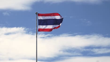 Waving-the-Kingdom-of-Thailand-flag-on-a-pole-with-blue-sky-and-white-clouds-in-the-background
