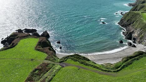 Copper-coast-Waterford-Ireland-static-shot-of-secret-beach-with-sea-cliffs-and-shimmering-sea-on-a-summer-day