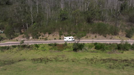 Aerial-tracking-shot-of-driving-campervan-on-empty-scenic-road,-near-Mallacoota,-Australia---Holiday-trip-in-woodland-of-Australia