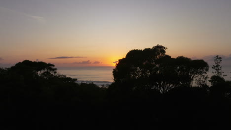 Luftpanorama-Mit-Wunderschönem-Sonnenuntergang-Hinter-Der-Silhouette-Von-Bäumen-Und-Meer-–-Drohnen-Weitwinkelaufnahme