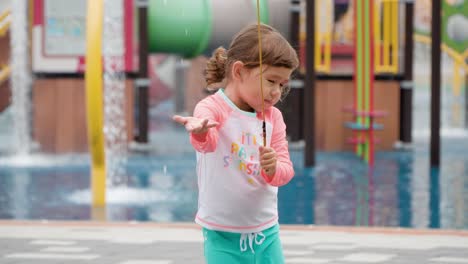 Adorable-Toddler-Girl-Playing-With-Water-at-Aqua-Playground,-Drags-Rope-To-Trigger-Waterfall-Shower,-Holds-Hand-Splashing