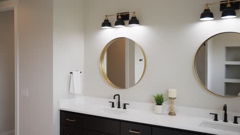 Medium-tight-shot-of-a-white-bathroom-sink-with-black-faucet,-white-countertops,-and-circular-mirror