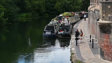 Two-Women-Walking-Past-Boast-On-The-Regants-Canal,-London,-United-Kingdom