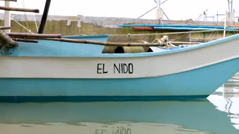 Colorful-traditional-Filipino-fishing-boat-with-hand-painted-El-Nido-moored-in-harbour-in-Palawan,-Philippines