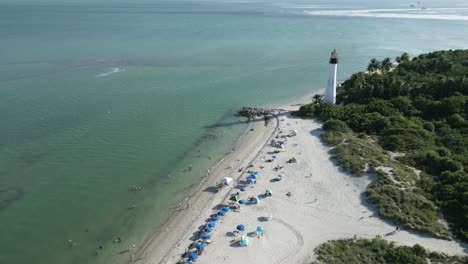 aerial-of-tropical-sand-white-beach-with-umbrella-in-Cape-Florida-Llighthouse-south-end-of-Key-Biscayne-in-Miami-Dade-County,-Florida-USA
