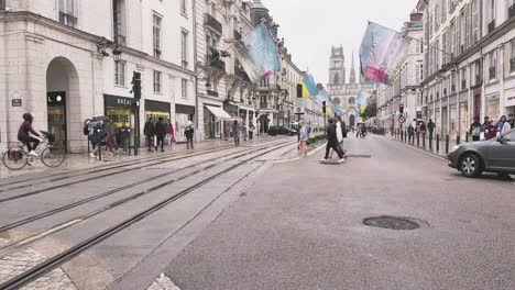 Crossing-the-street-with-tram-tracks-on-a-rainy-day-in-Orleans-France,-with-other-pedestrians
