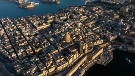Aerial-view-tilting-over-the-sunlit-coast-of-Valletta,-sunny-evening-in-Malta