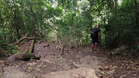 Male-with-flipflops-and-backpack-walks-down-stone-steps-in-forest