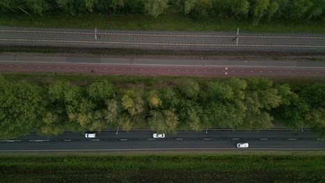 European-traffic-design:-top-shot-of-a-railroad,-bike-lane-and-a-road-for-cars-going-side-by-side-through-a-green-landscape