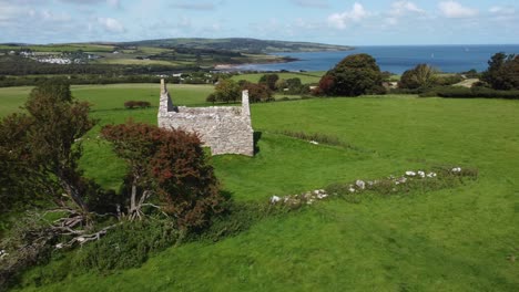 Establishing-countryside-aerial-view-over-Capel-Lligwy-ruined-chapel-on-Anglesey-island-coastline,-North-Wales