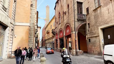 Tourists-Walking-and-Traffic-Driving-on-Cobblestone-Road-in-a-Bologna-Street