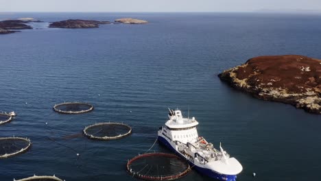 High-altitude-aerial-shot-of-a-fishing-well-boat,-a-fish-farm-and-the-sea
