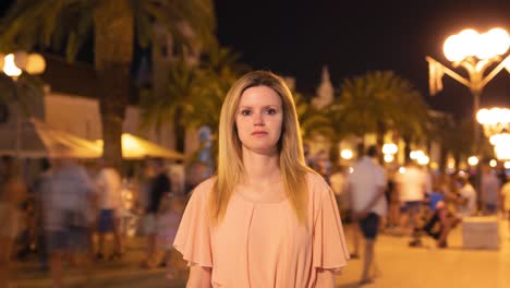 Time-lapse-shot-of-blond-woman-standing-on-crowded-promenade-in-Trogir-Croatia-at-night-during-holiday,-close-up