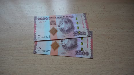 Cerca-De-Dos-Billetes-De-Chiles-Tanzanianos,-Dinero-En-La-Mesa-Con-Dibujo-De-León