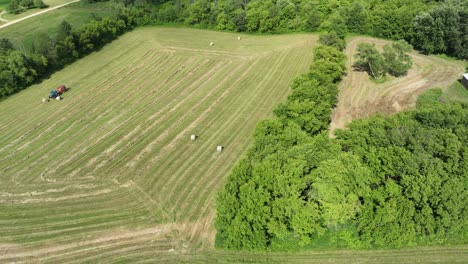 Farmer-bales-cut-summer-grass-into-hay-bales-in-Minnesota-field---Aerial-hyperlapse