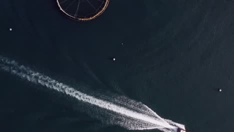 Bird's-eye-view-drone-shot-of-the-wake-of-a-fishing-boat-at-a-fish-farm