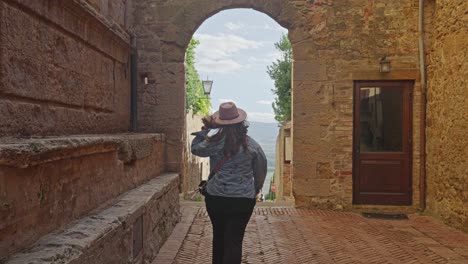 Female-Tourist-Walking-Towards-Archway-In-Pienza,-Tuscany,-Italy