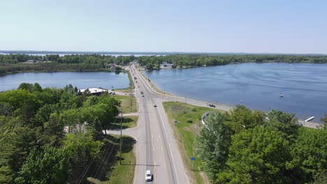Road-leading-to-small-town-of-Cadillac-over-lake-water,-aerial-drone-view