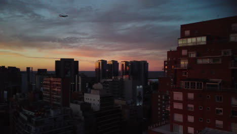 The-plane-flies-through-the-evening-sky-of-Buenos-Aires,-landing-over-the-city,-sunset,-blue-sky,-building,-drone-view