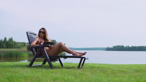 Beautiful-brunette-in-a-swimsuit-lying-on-a-sun-lounger-on-the-lake-smiling-working-remotely-via-the-Internet-in-the-business-sphere.-The-concept-of-country-life
